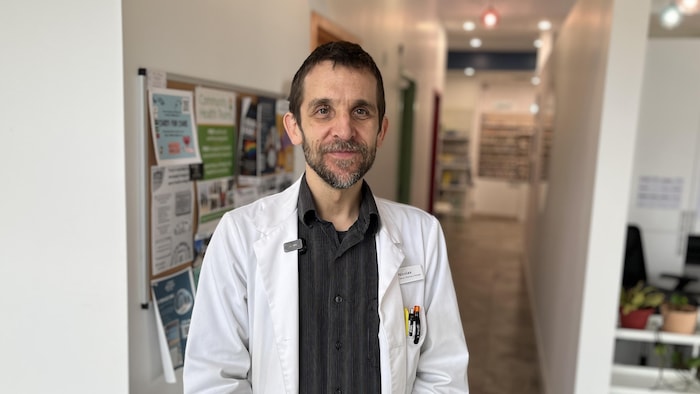 Un homme en sarrau blanc, debout dans une pharmacie.
