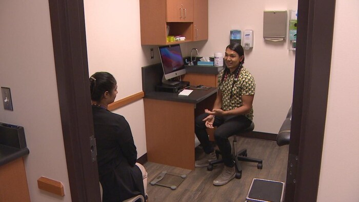 A man sitting at a computer in a clinic exam room speaks to a woman.