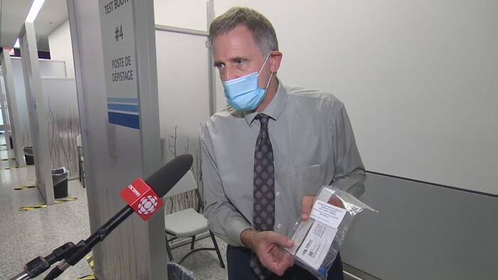 Un homme avec un masque montre un sac plastique dans lequel se trouve du matériel pour le dépistage de la COVID-19.