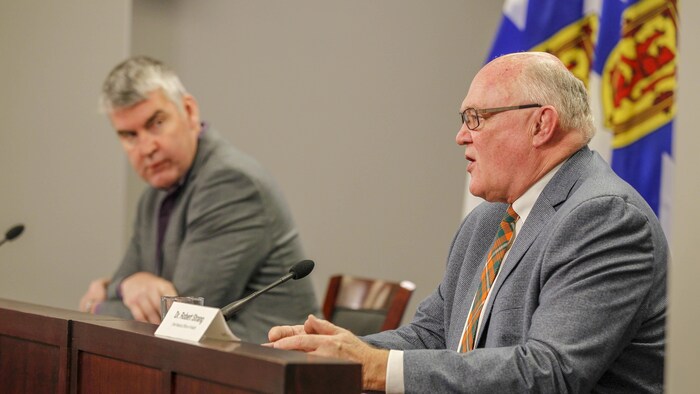 Robert Strang de profil et Stephen McNeil au loin qui le regarde.