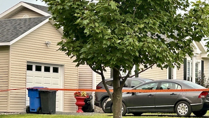 Police tape crosses the entire grounds of the residence where two vehicles are parked. 