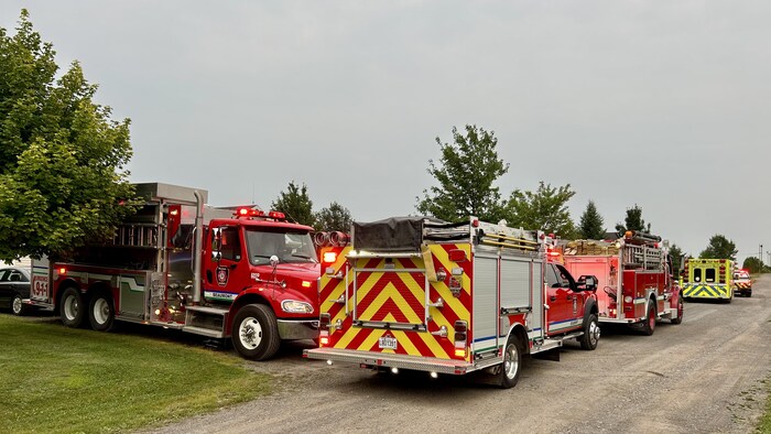 At least five emergency vehicles are on the side of a gravel road near a house.