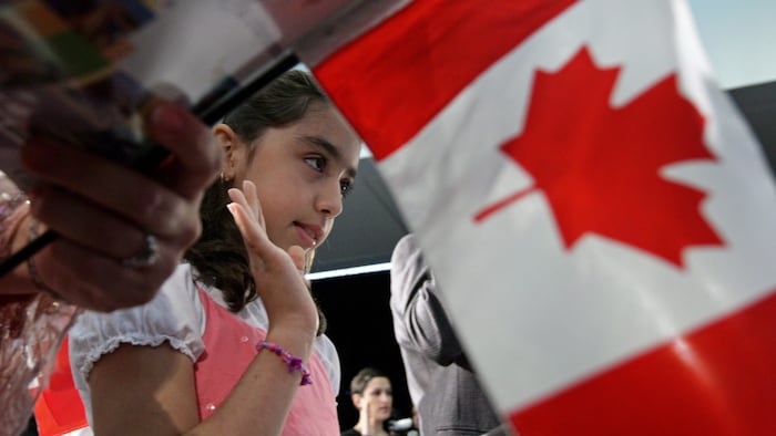 Une petite fille prête serment dans une cérémonie d'octroi de la citoyenneté canadienne, avec un drapeau canadien à l'avant-plan.
