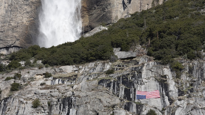 Un drapeau américain suspendu à l'envers sur une paroi rocheuse, près d'une chute.