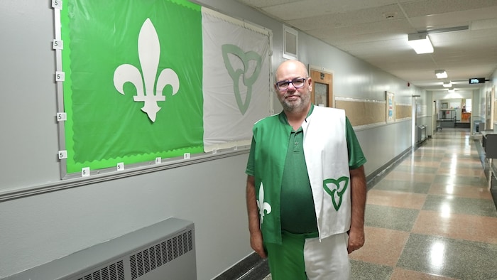 Devant le drapeau franco-ontarien qu’il a pris soin d’installer, Guy se tient dans le couloir de l’école.