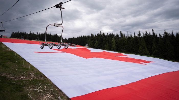 Un drapeau géant du Canada posé au sol sur une piste de ski.