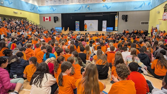 Plusieurs élèves portant des chandails orange dans un gymnase scolaire. 