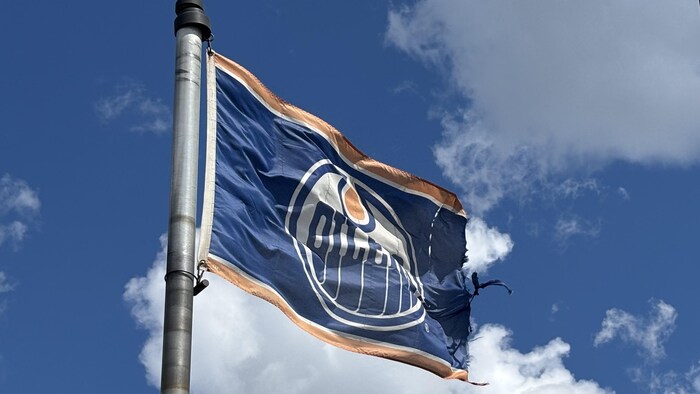 Un drapeau des Oilers d'Edmonton avec un ciel ennuagé en arrière-plan.