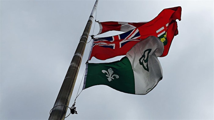 Le drapeau franco-ontarien, hissé en haut d'un mât aux côtés de ceux de l'Ontario et du Canada.