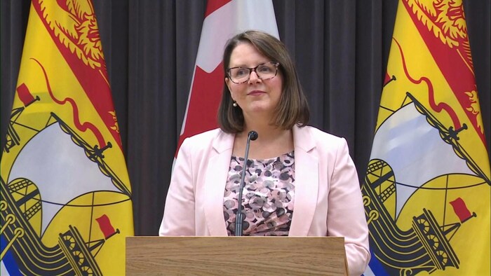 Jennifer Russell au micro, entre deux drapeaux du Nouveau-Brunswick.