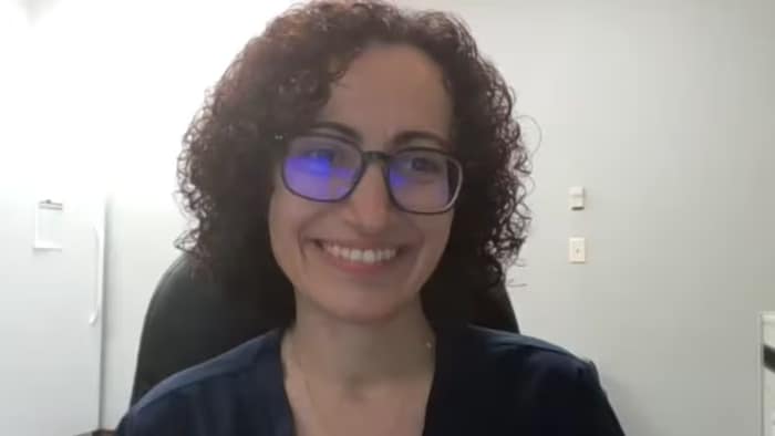 Une femme sourit devant l'objectif d'une caméra.
