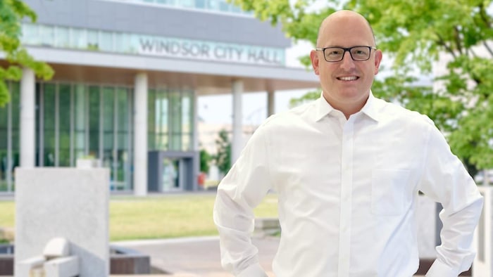 Drew Dilkens souriant pose en chemise devant l'hôtel de ville.
