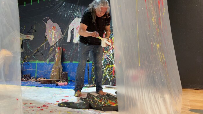 L’artiste Jacques Newashish tient de la peinture dans une pièce entourée de bâches de plastique.