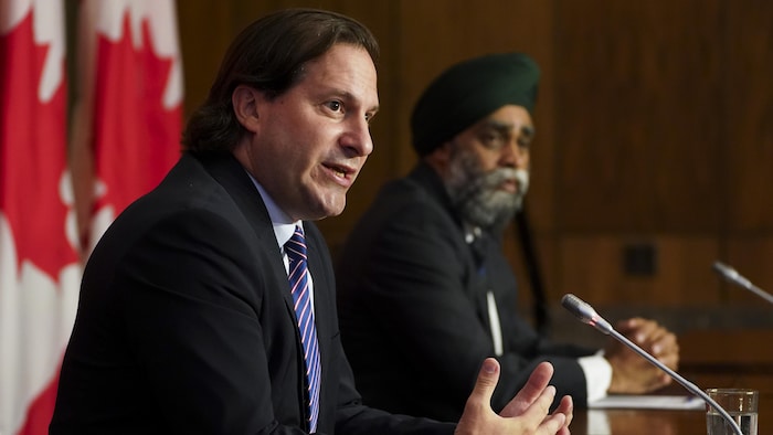 Marco Mendicino parle assis à la table de presse et Harjit Sajjan écoute.