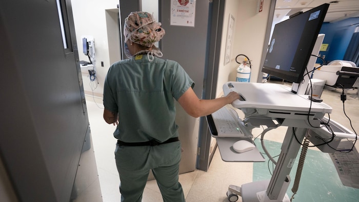 Une infirmière de dos entre franchit les portes d'une salle avec un ordinateur






