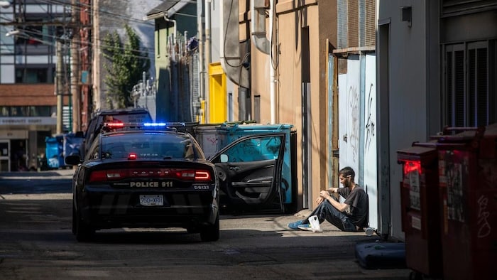 Une voiture de police dans une ruelle près d'un homme assis par terre.