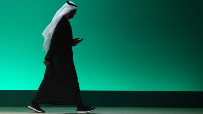 Un homme portant le thowb (robe) et l'agal (accessoire retenant le voile) traditionnels du Moyen-Orient marche en tenant un téléphone cellulaire.