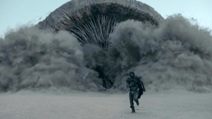 A person runs in front of a huge monster.