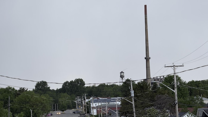 Une grande cheminée industrielle et un château d'eau avec un village en avant-plan.