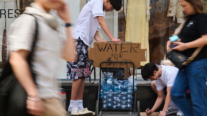Des piétons croisent des vendeurs d'eau par une chaude journée devant le centre Eaton, à l'intersection de Yonge et Dundas à Toronto.