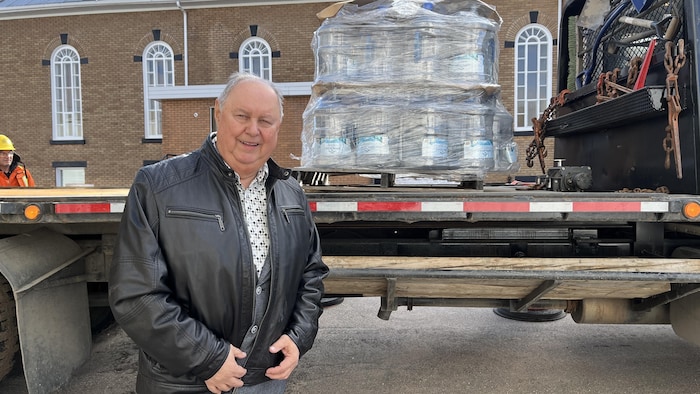 Rémi Rousseau se tient devant un emballage de bidons d'eau.