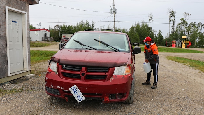 Une dame de 65 ans porte un bidon vers sa vieille auto rouge dans une communauté autochtone du nord de l'Ontario