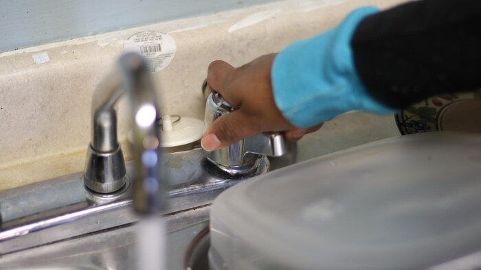 Une main de femme qui ouvre un robinet d'où coule de l'eau.