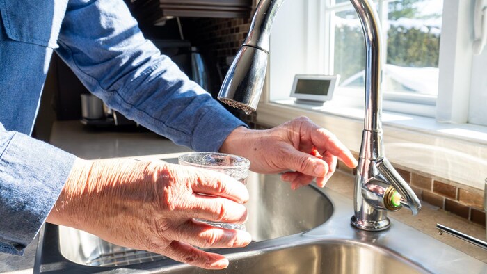Une main qui ouvre un robinet et une autre qui tient le verre.