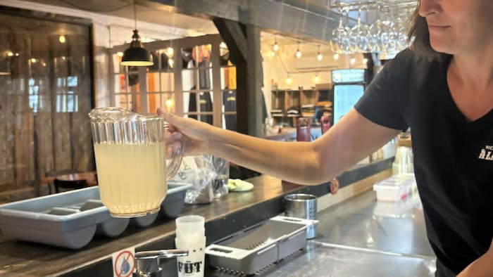 Une femme dans un restaurant tient un pichet d'eau de couleur brunâtre