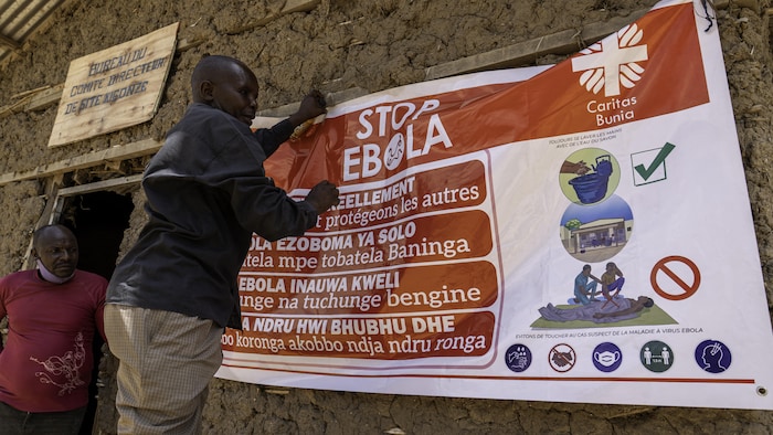 Un homme accroche une affiche de mesures pour empêcher la transmission du virus Ebola.