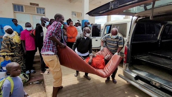Des gens sortent un malade couché sur un matelas d'une camionnette.