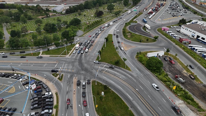 Photo aérienne de l'intersection de trois artères majeures, dont une à l'horizontale entre un cimetière et la cour d'un concessionnaire automobile.