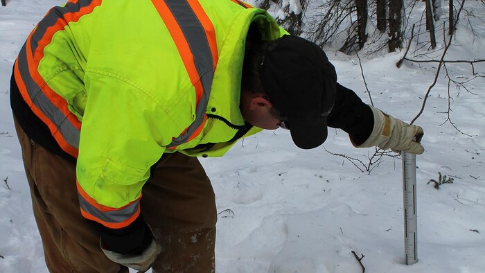 un homme qui place le cylindre métallique dans la neige.