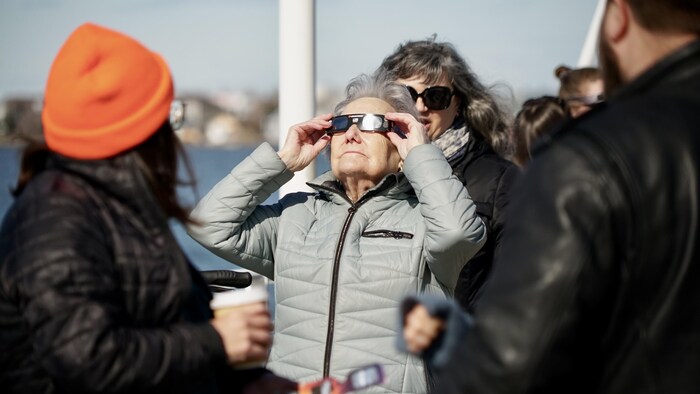 Une dame regarde l'éclipse avec ses lunettes.             