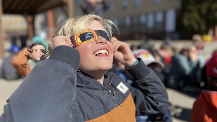 Un jeune homme regarde l'éclipse avec des lunettes.