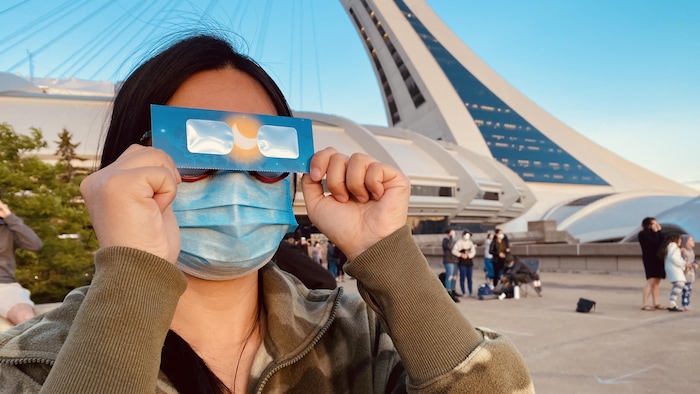 Une femme protège ses yeux avec des lunettes spéciales pour observer l'éclipse près du stade.