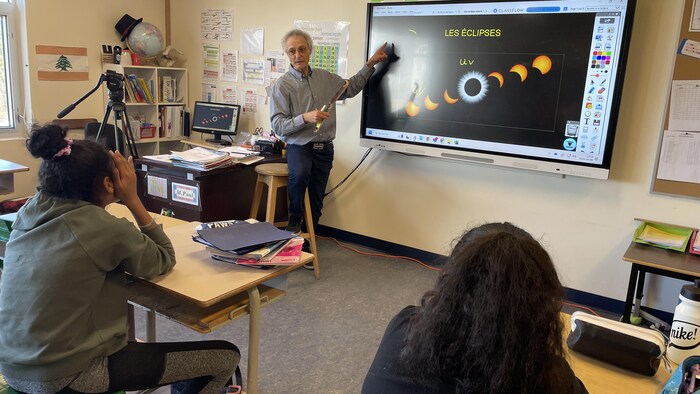 L'enseignant Paul Beau présente les phases d'une éclipse solaire sur un tableau interactif devant une classe.