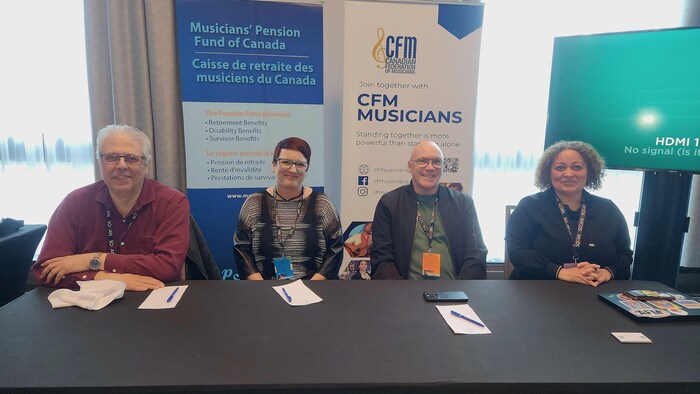 Quatre personnes assises derrière une table. Derrière eux, une banderole indiquant le logo de la Fédération canadienne des musiciens.