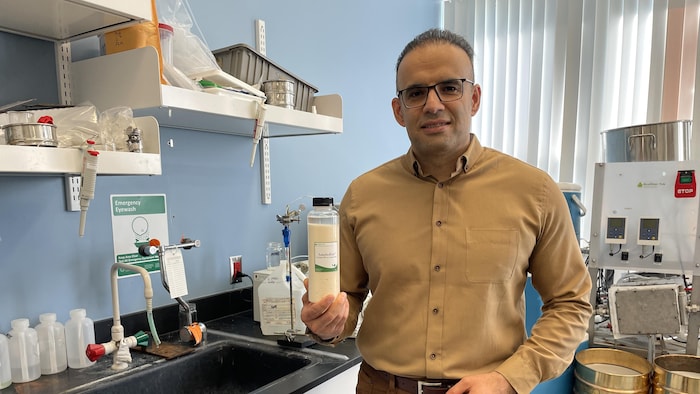 Un homme tenant une bouteille remplie de résine dans un laboratoire.