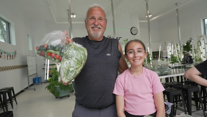 Un homme tient un sac de salade avec une jeune fille à ses côtés.