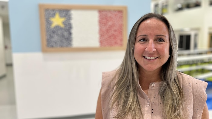 Une femme souriante devant une mosaïque de céramique formant un drapeau acadien. 