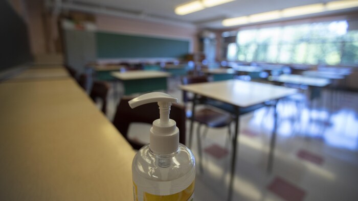 Une classe vide avec, en avant-plan, une bouteille de désinfectant.