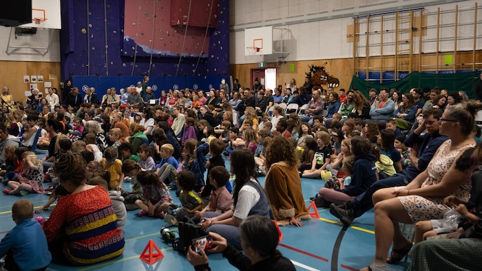 Beaucoup de monde assis par terre ou sur des chaises dans le gymnase de l'École Émilie-Tremblay, à Whitehorse.