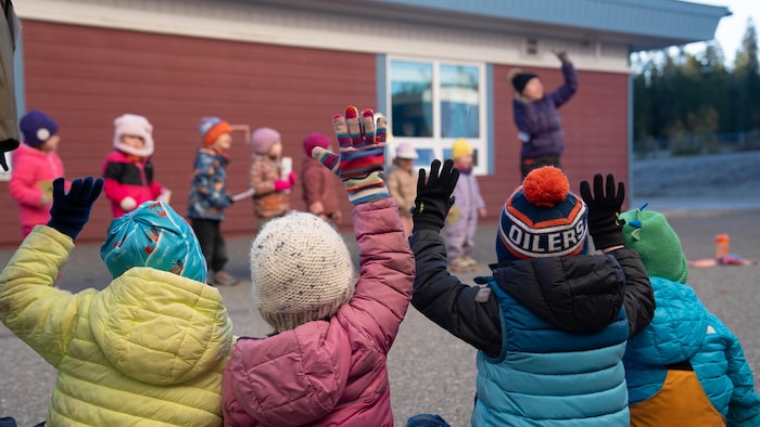 Des enfants sont assis dans la cour de récréation et miment des chiffres avec leurs doigts devant leur enseignante.