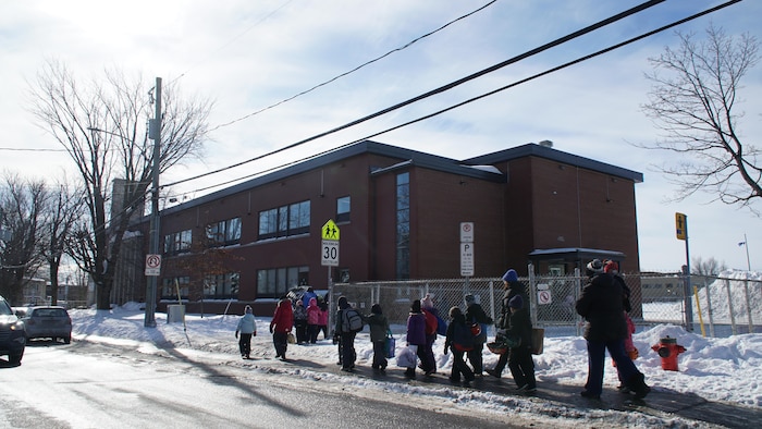 Des élèves en habit d'hiver marches vers une école, dans la neige. 