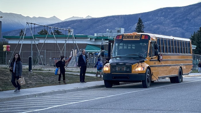 Un bus scolaire avec des jeunes, des enfants, des adultes devant l'école Desrochers de Jasper, en septembre 2024.