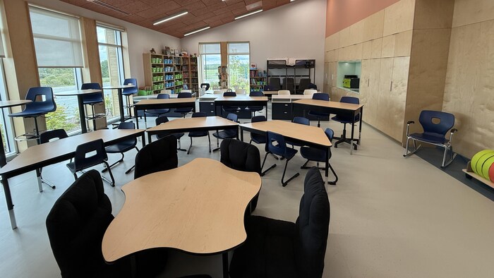 Des petites tables disposées dans une classe munie de grandes fenêtres.