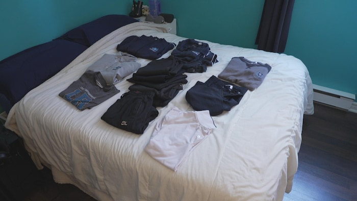 Des vêtements aux couleurs de l'École Louis-Riel disposés sur un lit.