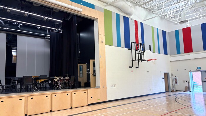 Un panier de basketball dans un gymnase scolaire et une estrade avec des projecteurs au-dessus.
