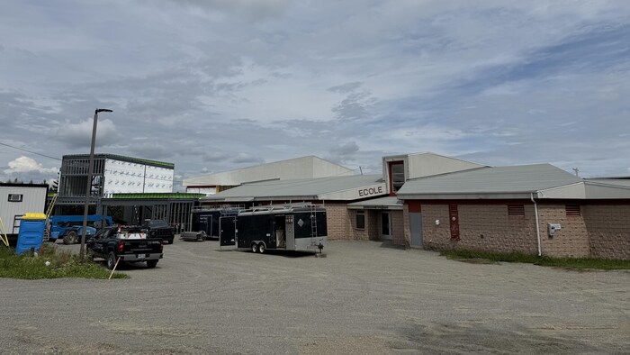 Des véhicules stationnés derrière un bâtiment en construction et une école.